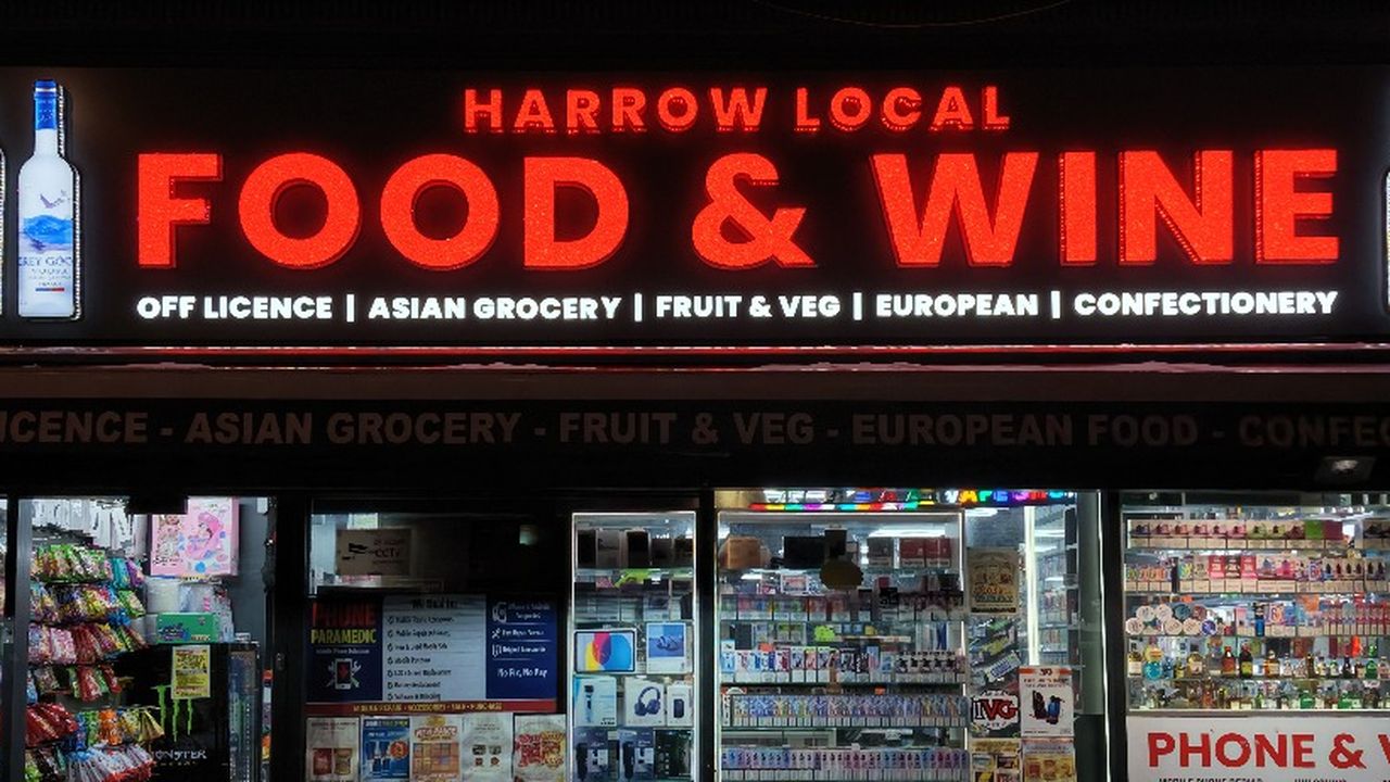 The same Harrow Local Food & Wine shop front at night, red crystal letters glowing